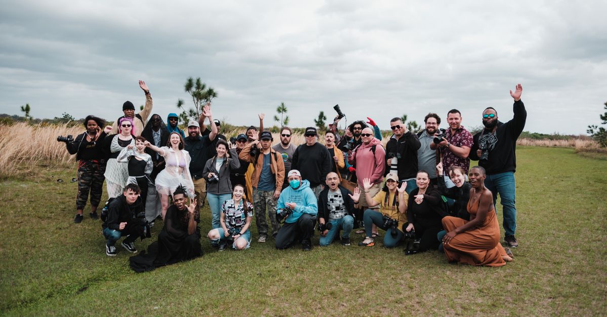 A diverse group of photographers posing together in a natural setting with cameras.